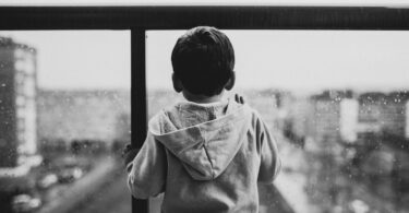 backview of sad child waiting on a glass window